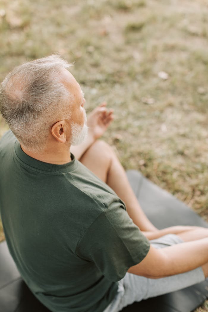 A senior man practices meditation in a serene park setting, focusing on breathing and wellness.
